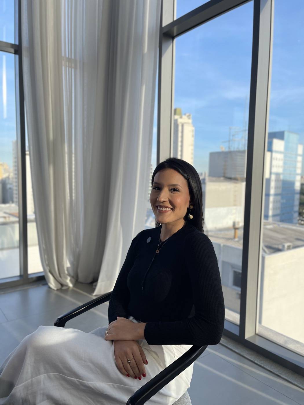 Jéssica Galvani junto à janela de um escritório com vista para a cidade